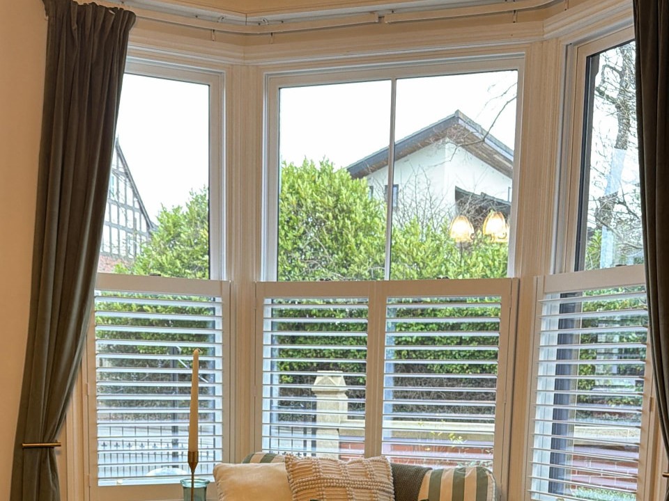 White plantation shutters with 63mm slats tilted open in a bright Manchester living room