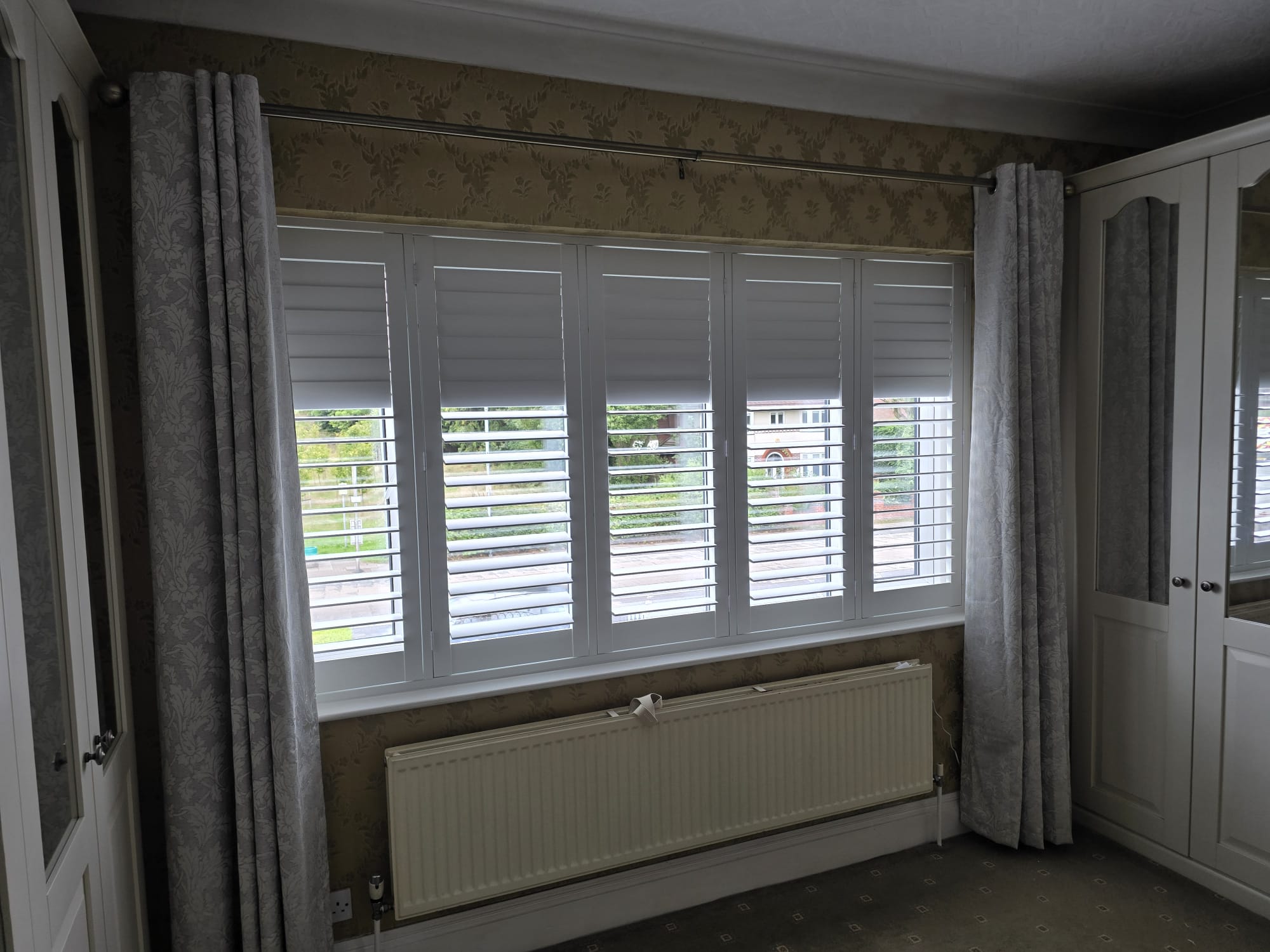 White plantation shutters with curtains in a Manchester bedroom