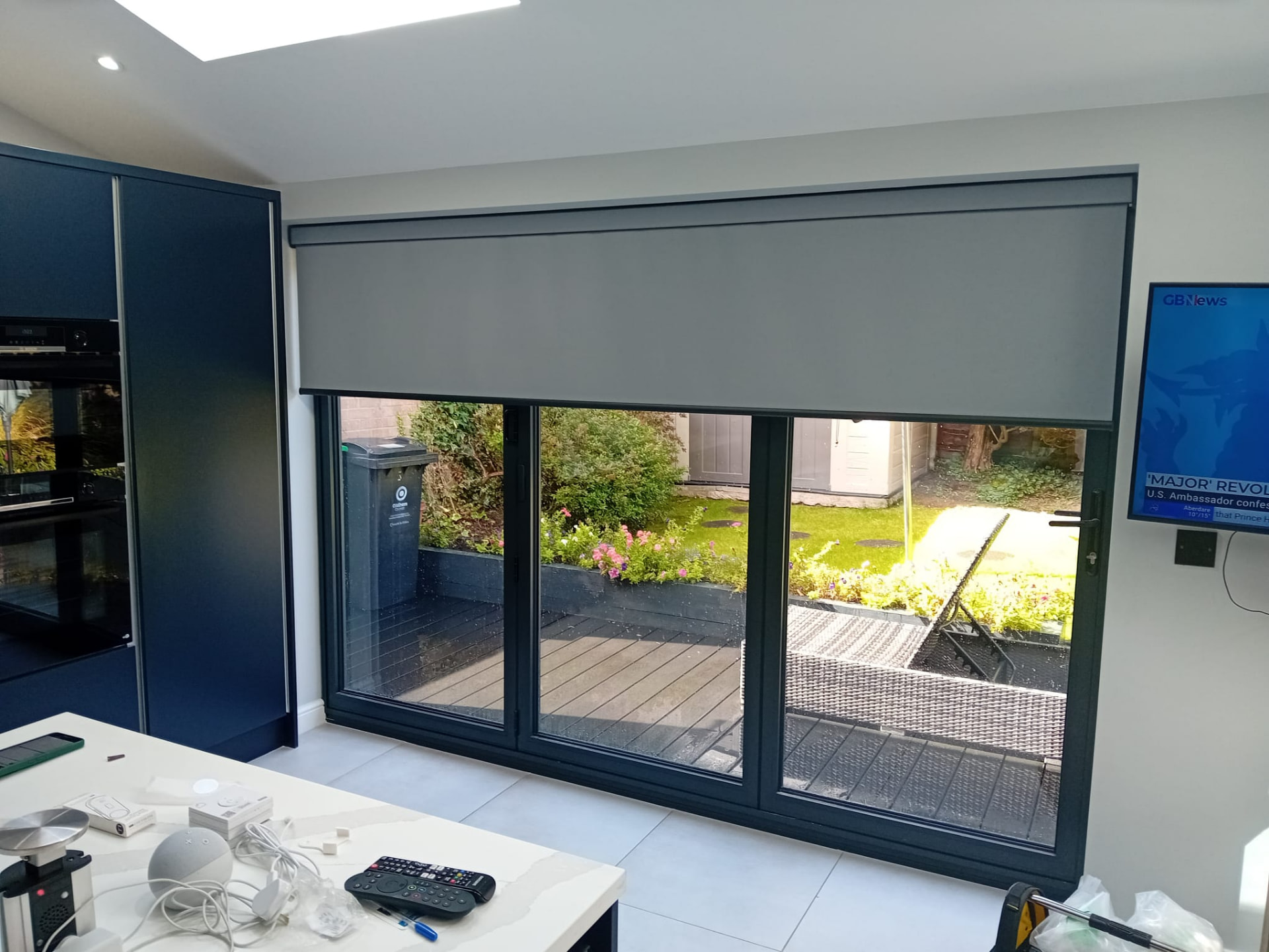 Grey roller blind fitted across three-panel bi-fold doors in a kitchen