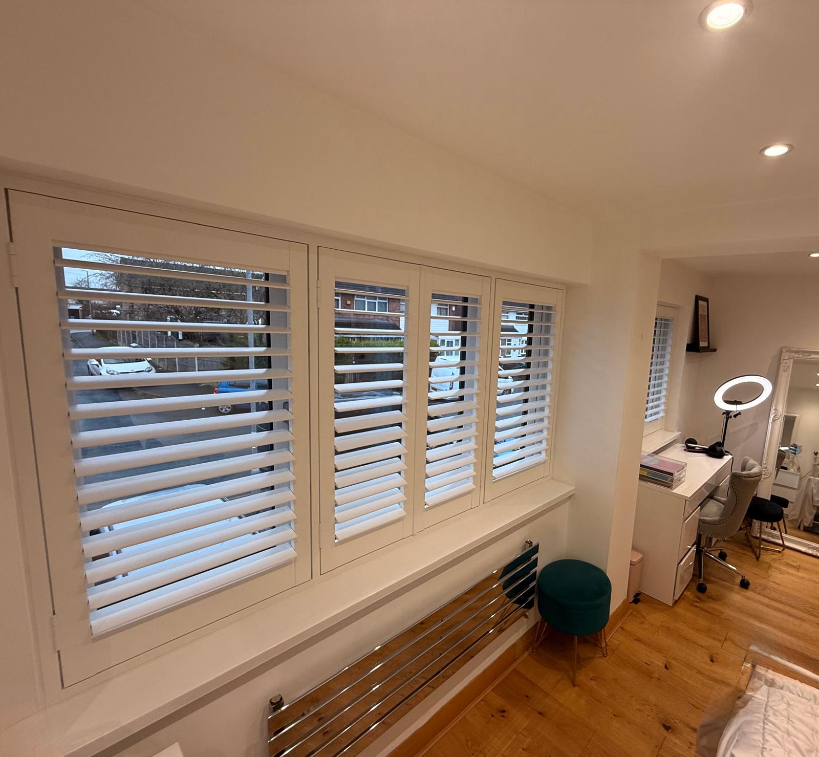 White full-height plantation shutters fitted across a bedroom window with a smaller shuttered window in a nook